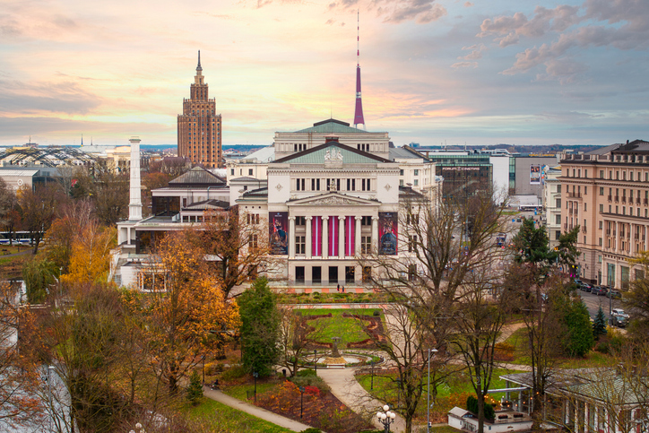 Ein repräsentatives Gebäude steht vor einem Park mit Wegen und herbstlichen Bäumen.