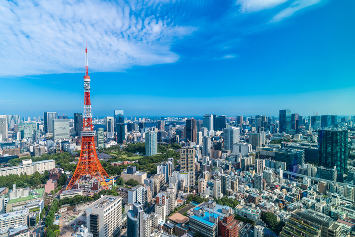Über der dichten Stadtlandschaft von Tokio ragt der rotweiße Tokio Tower unter blauem Himmel empor.