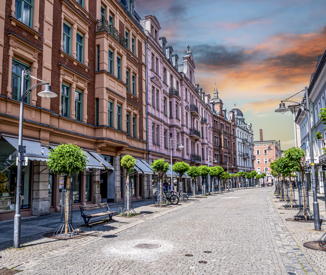 Straßenzug mit aufwendig verzierten historischen Gebäuden unter einem farbenfrohen Abendhimmel.