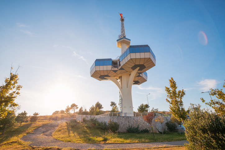 Ein moderner Aussichtsturm steht auf einer kleinen Anhöhe in warmem Sonnenlicht.
