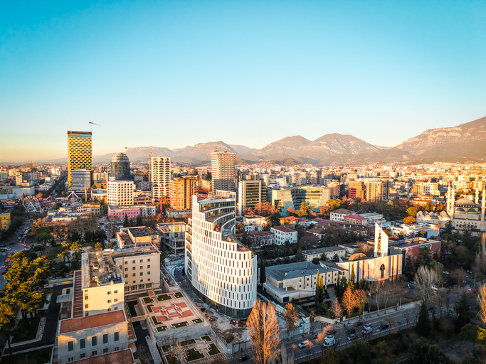 Drohnenaufnahme der Stadt Tirana mit modernen Hochhäusern und Kirchen während der goldenen Stunde.