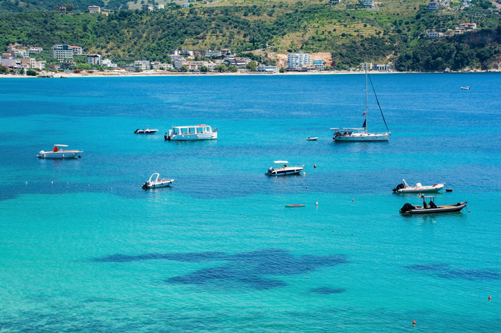 Mehrere kleine Boote und eine Yacht liegen auf türkisblauem Wasser vor einer grünen Küste.