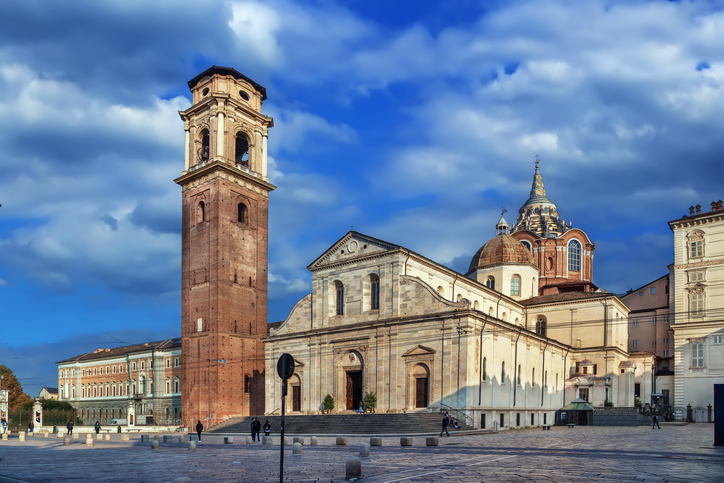 Ein hoher Backsteinturm steht neben einer großen Kirche auf einem weiten Platz.