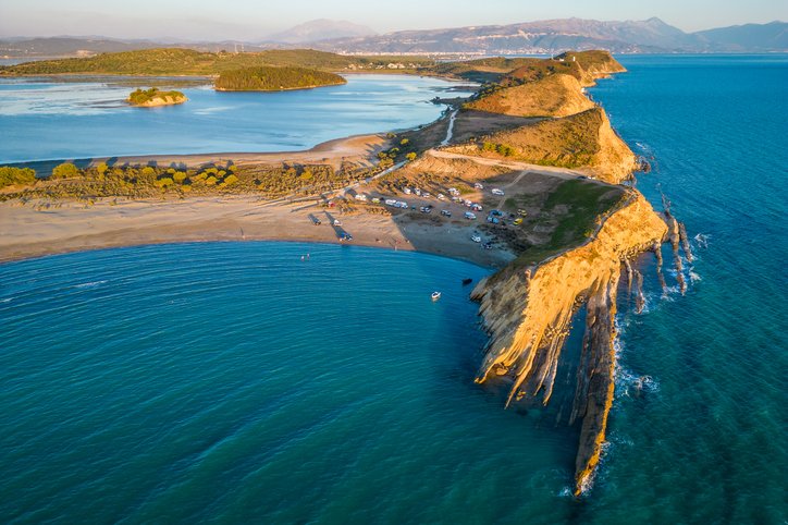 Eine schmale Landzunge ragt zwischen blauem Meer und ruhiger Lagune in die weite Küstenlandschaft hinein.