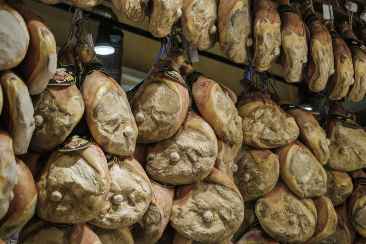 Viele große Schinken hängen dicht nebeneinander in einem Innenraum.