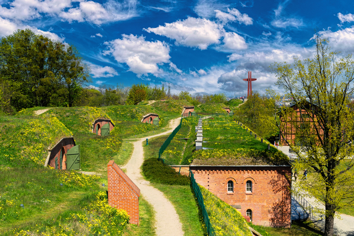 Begrünte Wälle, Wege und kleine Backsteingebäude ziehen sich durch eine offene Parklandschaft.