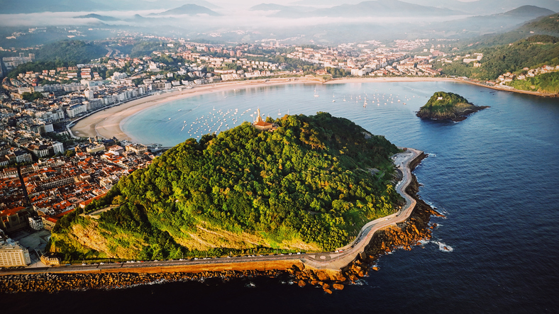 Eine Luftaufnahme zeigt eine grüne Insel vor einer halbkreisförmigen Küste.