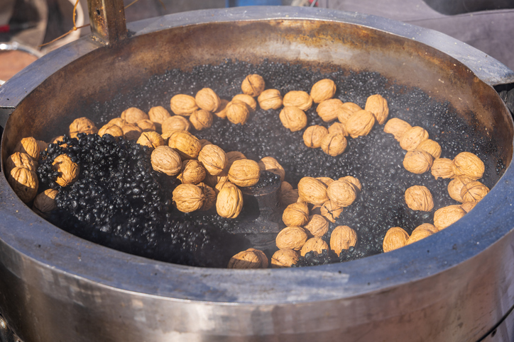 Frische Walnüsse werden in einem großen, runden Metallbehälter über dunklen Steinen geröstet.