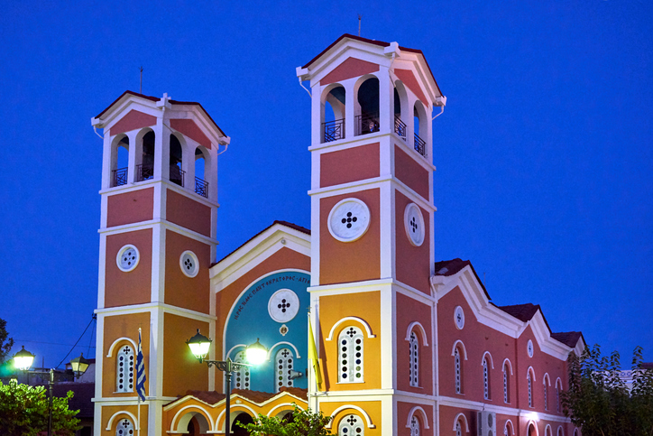 Eine prächtige, rot-orange beleuchtete Kirche mit zwei markanten Glockentürmen unter einem dunkelblauen Abendhimmel.