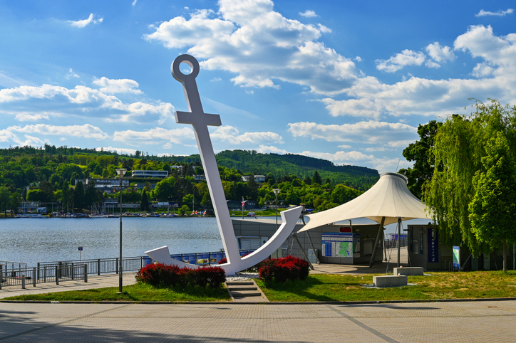 Ein weißer Anker steht an einer Promenade direkt am Wasser.