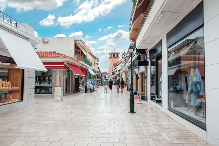 Eine helle, moderne Fußgängerzone mit exklusiven Geschäften und weiß bespannten Markisen unter einem blauweißen Wolkenhimmel.
