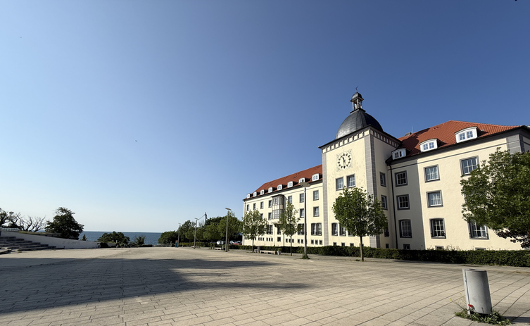 Ein imposantes, hellgelbes Gebäude mit rotem Dach und einem markanten Uhrturm unter strahlend blauem Himmel.