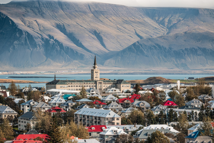 Stadtansicht von Reykjavík mit farbenfrohen Hausdächern, einer markanten Kirche und massiven Bergen im Hintergrund.