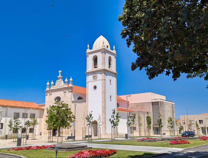 Große weiße Kirche mit Uhrenturm und Kreuz vor strahlend blauem Himmel.