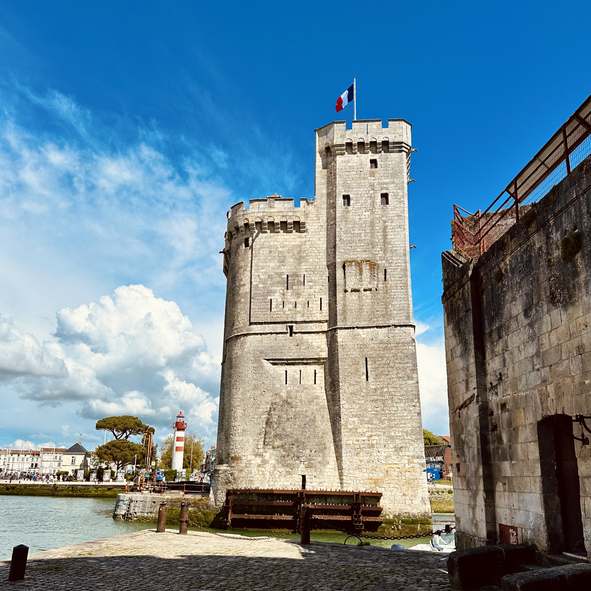 Ein hoher, mittelalterlicher Steinturm mit französischer Flagge direkt am Wasser unter blauem Himmel.