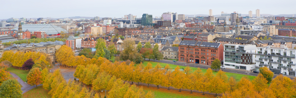 Ein weiter Blick über eine herbstlich gefärbte Allee im Glasgow Green auf die Silhouette der umliegenden Stadtviertel.