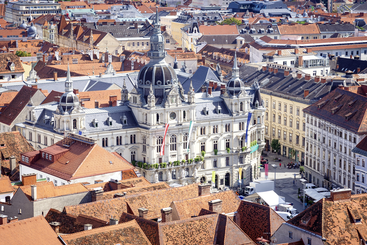 Ein prachtvolles, helles Rathaus mit mehreren Türmen und Flaggen, umgeben von den typischen roten Ziegeldächern.