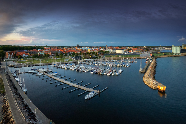 Luftaufnahme des Yachthafens bei Dämmerung mit zahlreichen Segelbooten an den Stegen und der Stadt im Hintergrund.
