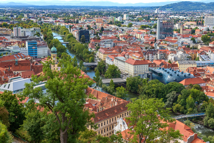 Eine Ansicht von oben auf den Fluss Mur, der durch Graz fließt, mit dem blauen, futuristischen Kunsthaus am Ufer.