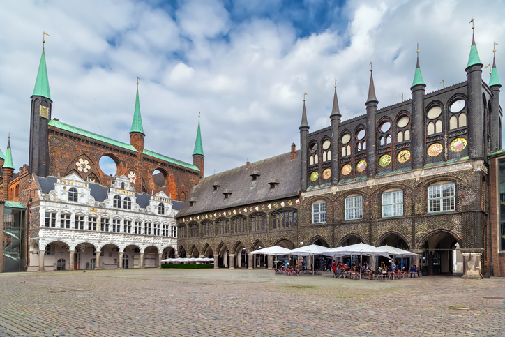 Die prachtvolle Schaufassade des Rathauses mit dunklen, glasierten Ziegeln, hohen Windlöchern und weißen Arkaden unter einem wolkigen Himmel.