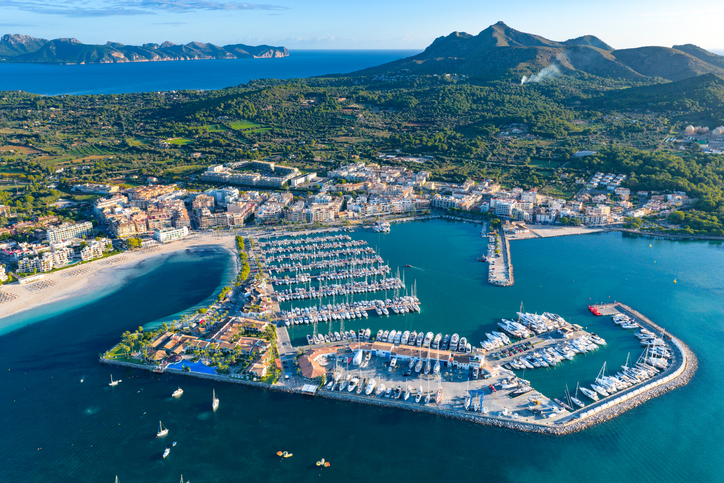 Aus der Vogelperspektive sind der Yachthafen, der Strand und die Küstenlinie mit türkisblauem Wasser zu sehen.