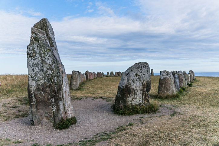 Große, aufrecht stehende Steine einer monumentalen Schiffssetzung auf einer grasbewachsenen Klippe über dem Meer.