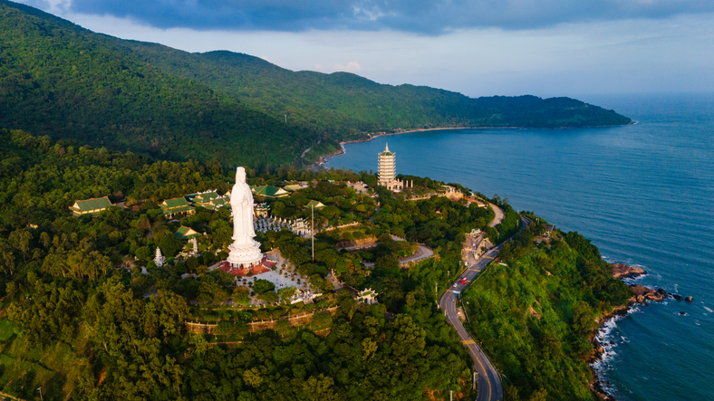 Eine riesige weiße Buddha-Statue auf einem bewaldeten Hügel direkt an der tiefblauen Küste von Da Nang.