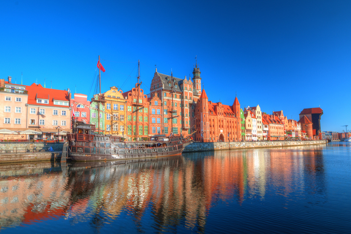 Bunte historische Speicherhäuser und ein Schiff spiegeln sich im ruhigen Wasser.