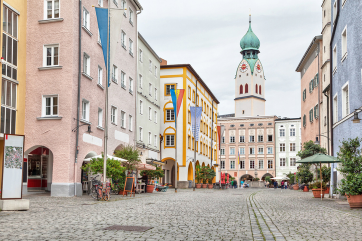 Ein gepflasterter Marktplatz mit bunten Häusern und dem markanten grünen Zwiebelturm der Heilig-Geist-Kirche.
