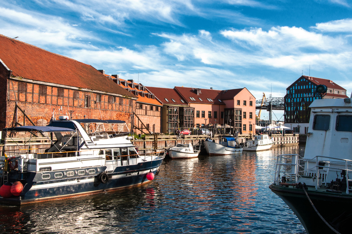 Boote liegen vor Backstein- und Fachwerkhäusern an einem ruhigen Wasserarm.