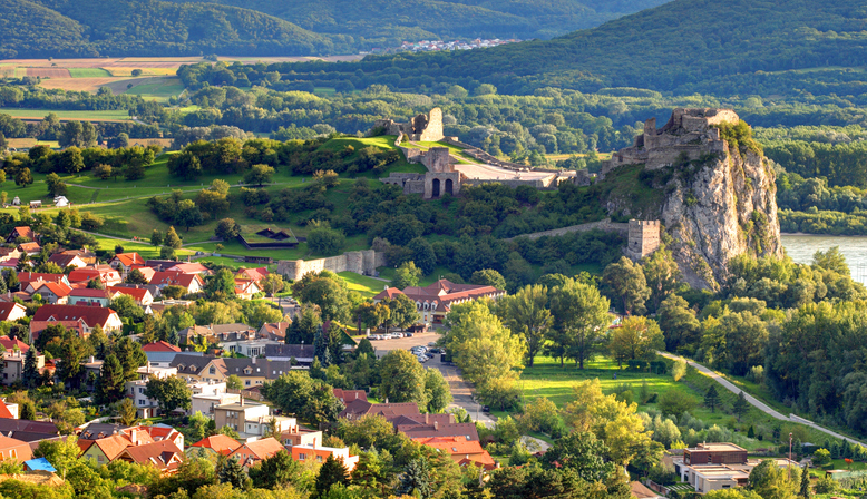 Über einer grünen Landschaft erhebt sich eine Burgruine auf einem felsigen Hügel.