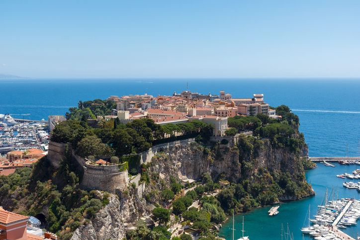 Ein Panorama-Blick auf den massiven Felsen von Monaco, auf dem die historische Altstadt und der Palast thronen, umgeben von türkisblauem Wasser.