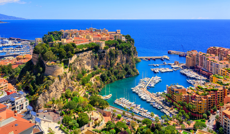 Ein Panoramablick auf den massiven Felsen von Monaco, auf dem die Altstadt thront, daneben der Jachthafen von Fontvieille in tiefblauem Wasser.