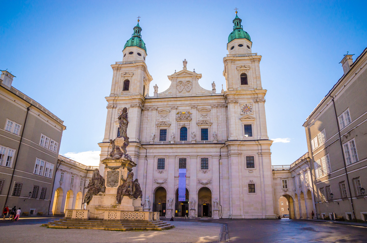 Eine große barocke Kirche mit zwei Türmen steht auf einem gepflasterten Platz.
