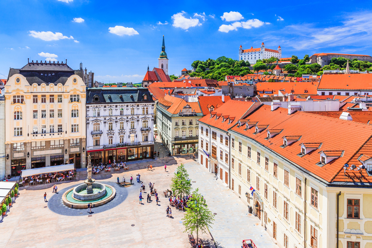 Ein weiter Platz mit Brunnen und historischen Häusern liegt unterhalb einer Burg auf dem Hügel.
