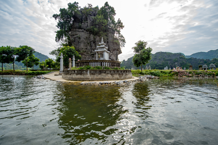 Ein kleiner weißer Altar auf einer runden Plattform im Wasser vor einer massiven Felswand.