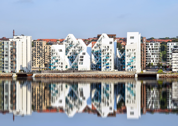 Das markante, weiße "Isbjerget" Wohngebäude in Aarhus, dessen spitze Dächer sich perfekt im ruhigen Wasser spiegeln.