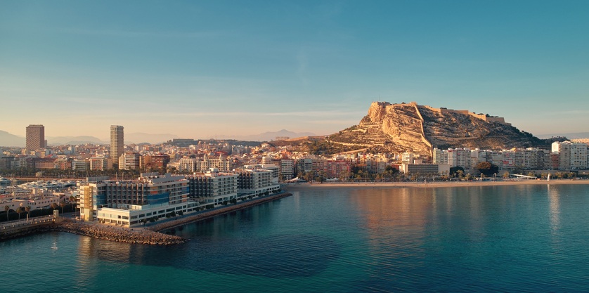 Blick auf den Yachthafen und das imposante Castillo de Santa Bárbara über der Stadt Alicante im warmen Abendlicht