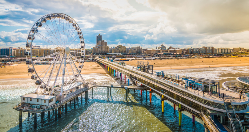 Luftaufnahme des berühmten Piers von Scheveningen mit einem großen weißen Riesenrad über der Nordsee bei sonnigem Wetter.