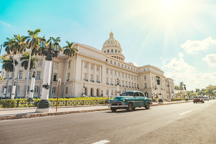 Ein klassischer türkisfarbener Oldtimer fährt bei hellem Sonnenschein am imposanten Capitolio Nacional in Havanna vorbei.