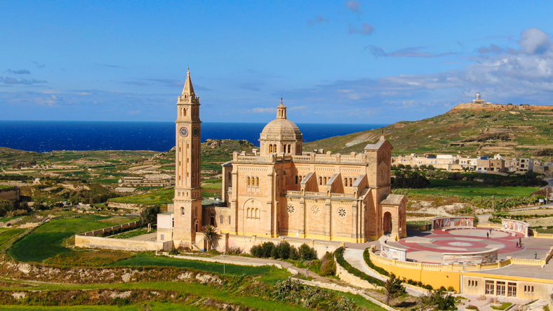 Die monumentale Wallfahrtskirche Ta' Pinu steht majestätisch in der grünen Hügellandschaft von Gozo vor dem Meer.