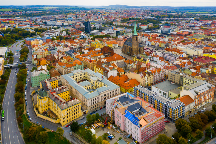 Luftaufnahme über ein großes, helles Gebäudeensemble mit Innenhöfen, angrenzend an moderne Stadtviertel und eine breite Ausfallstraße.