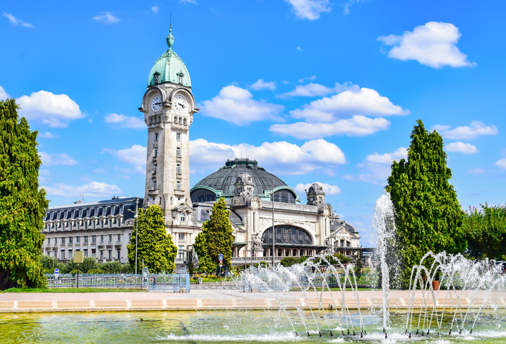 Der Bahnhof Limoges Bénédictins mit Uhrturm, Kuppel und Wasserspielen an einem sonnigen Tag.