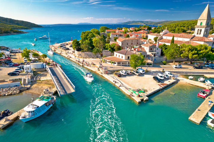 Blick von oben auf den schmalen Kanal bei Osor auf Cres, durch den gerade ein Boot fährt, mit Blick auf das offene Meer.