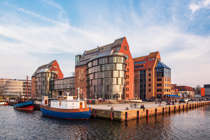 Ein blau-weißes Boot liegt am Kai vor modernen Backsteingebäuden mit großen Glasfronten während der goldenen Stunde.