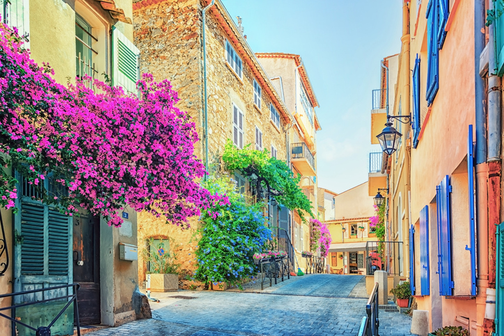 Eine sonnige, enge Straße in Saint-Tropez mit farbenfrohen Häusern und üppigen Bougainvillea-Blüten