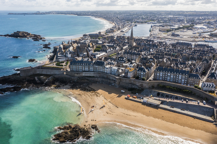 Luftaufnahme der hellen Sandstrände von Saint-Malo mit der massiven Stadtmauer und den grauen Granithäusern direkt dahinter.