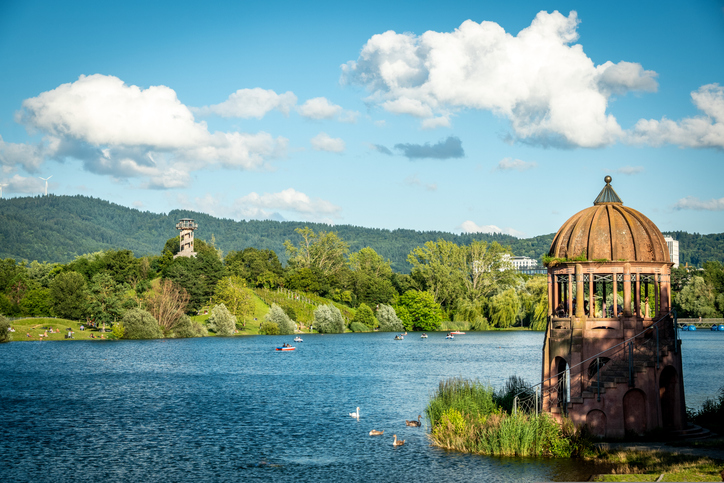 Blick über den Flückigersee im Seepark Freiburg mit einem kleinen Pavillon am Ufer.