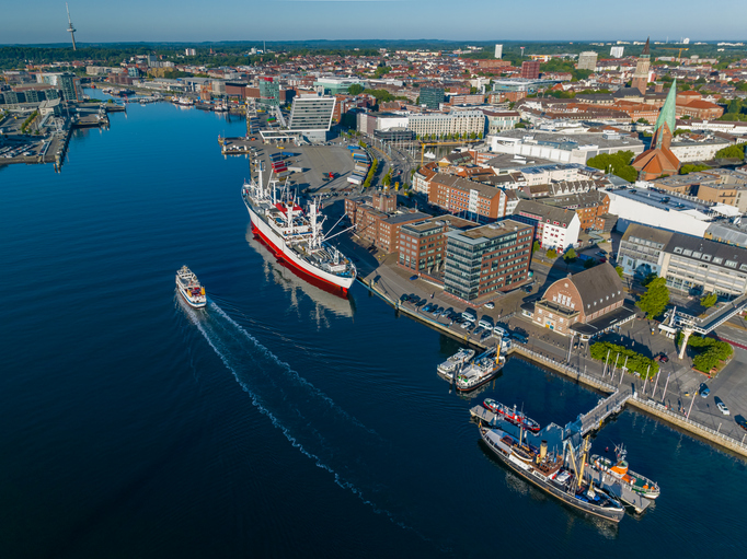Luftbild von Kiel mit Hafenanlagen, großen Schiffen, Innenstadt und Wasserflächen der Kieler Förde.