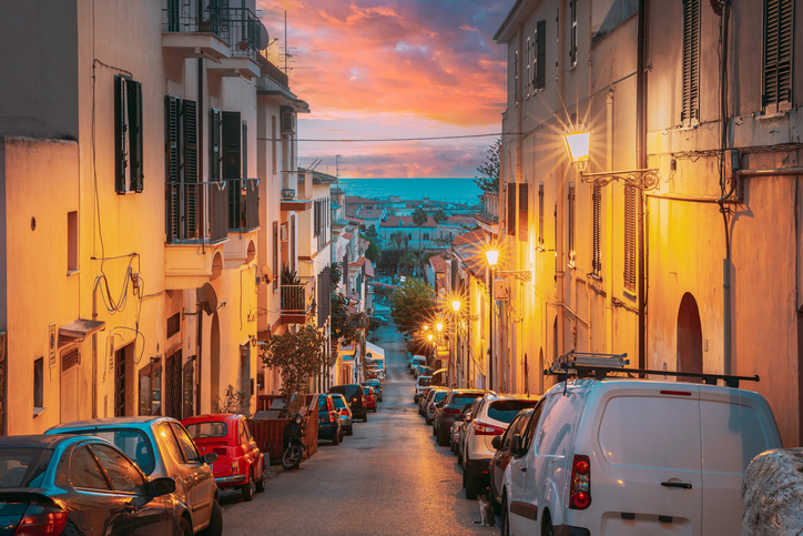Eine schmale, abfallende Straße in Terracina während eines dramatischen, farbenfrohen Sonnenuntergangs mit Blick auf das Meer.